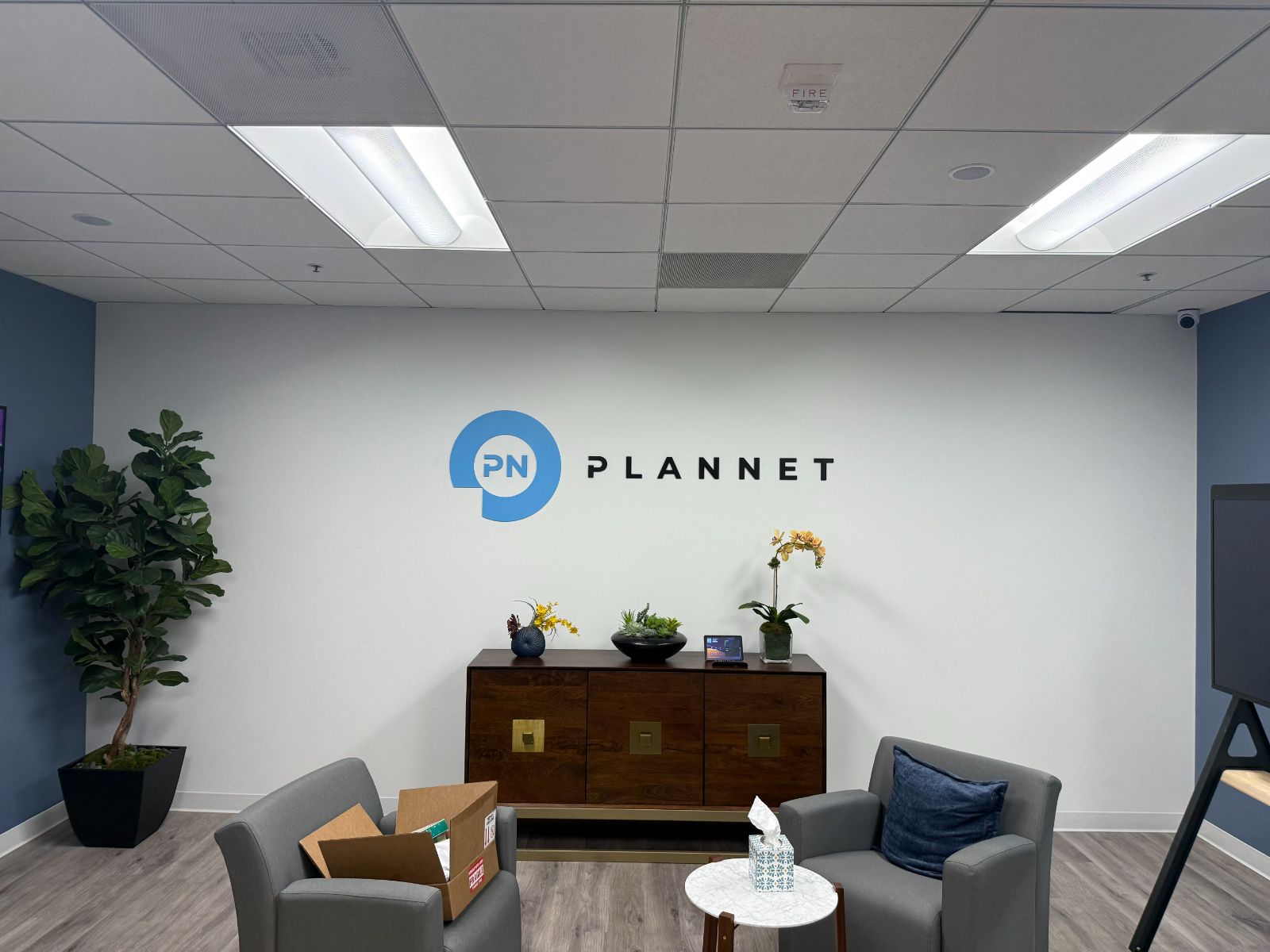 Reception wall with the PLANNET logo in flat-cut acrylic letters above a wood credenza