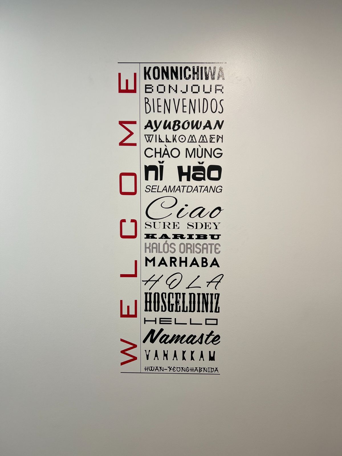 Multi-language welcome wall graphic: red cut vinyl WELCOME letters beside greetings in 18 languages