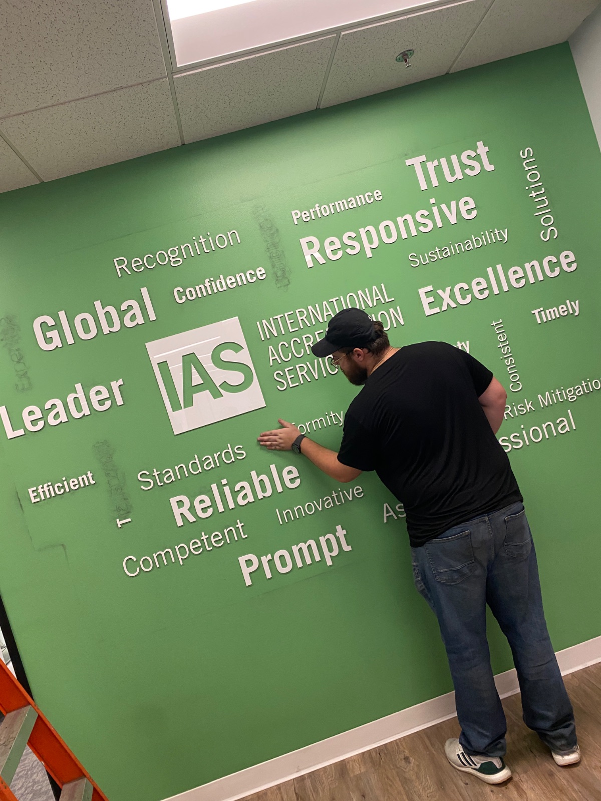 Installer squeegeeing a cut-vinyl word panel onto the green wall during application